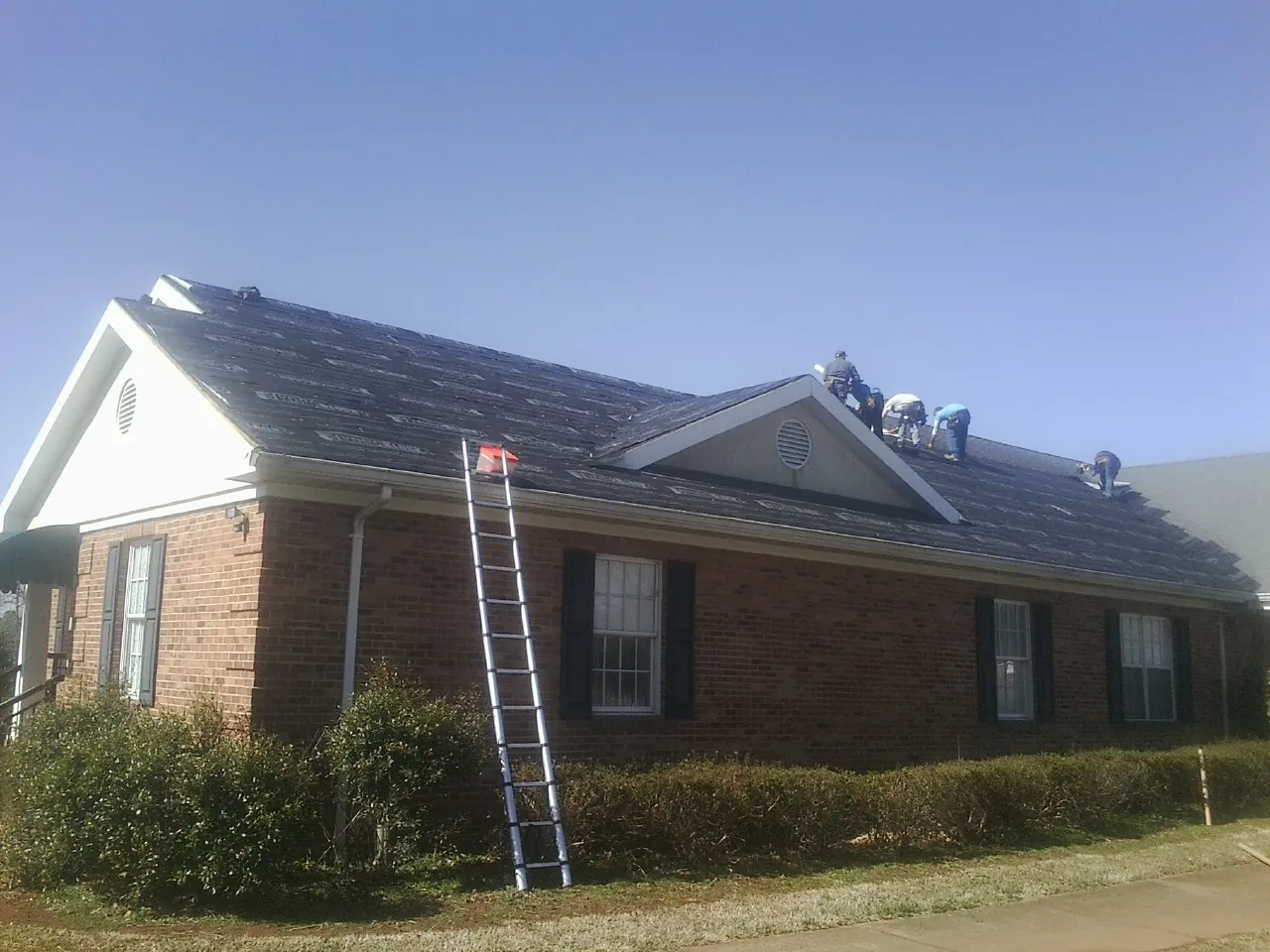 Crew tearing shingles off a brick ranch roof with a ladder set — Metal Roof Repair work by our crew in Lima