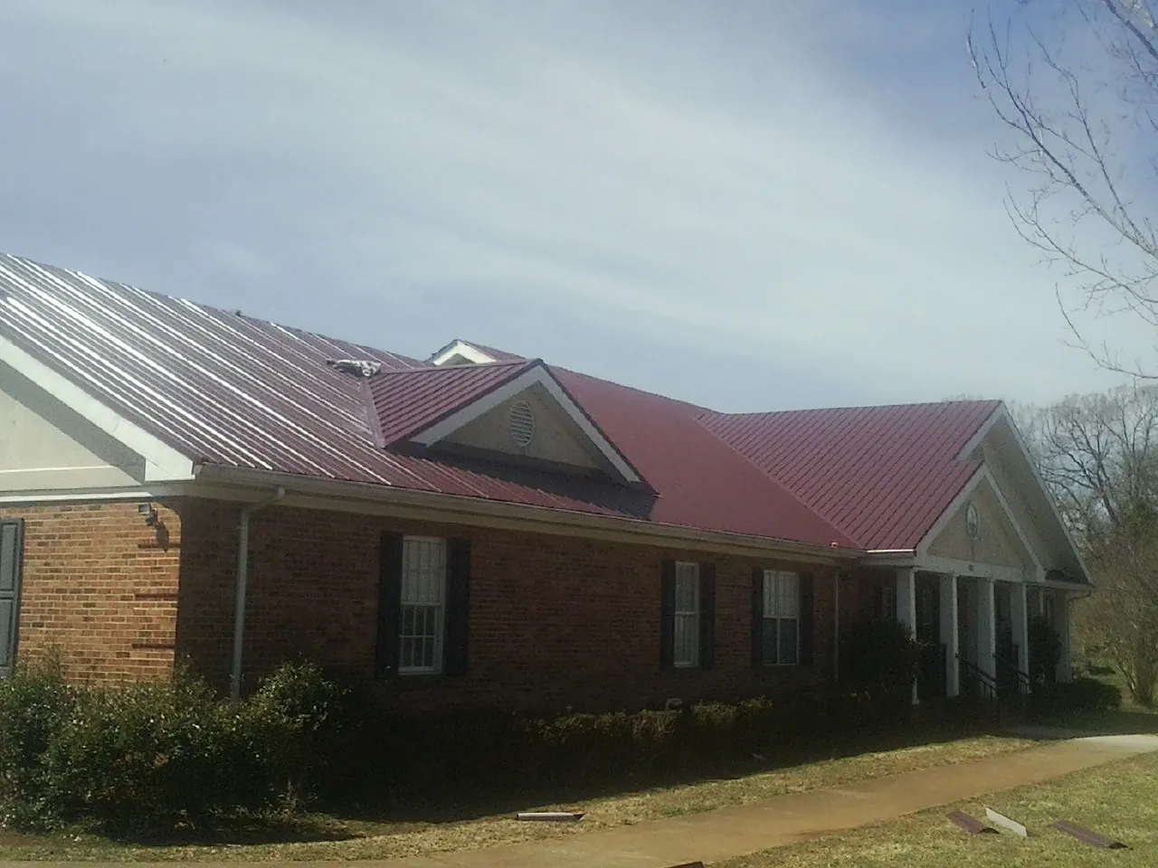 Red metal roof with gabled entries on a long brick building, from a Hail Damage Roof Repair job in Lima
