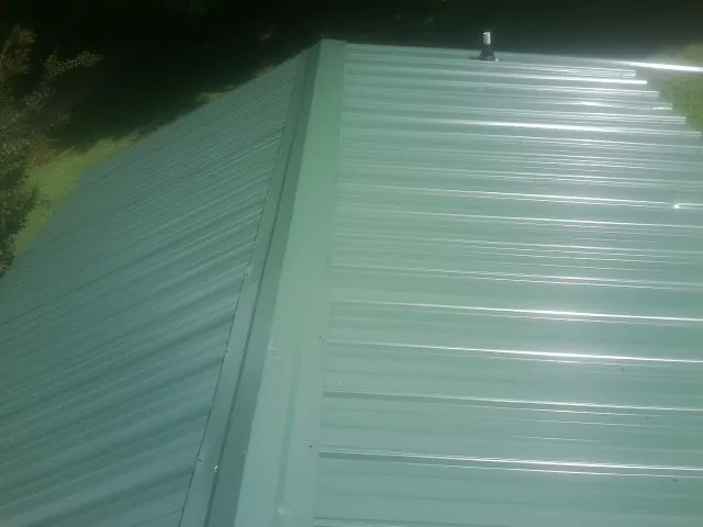 New green metal panels meeting at the ridge of a roof — Flat Roof Repair work by our crew in Lima