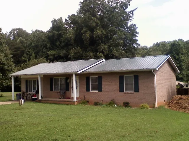 Gray metal roof on a brick ranch house with a side carport in Lima