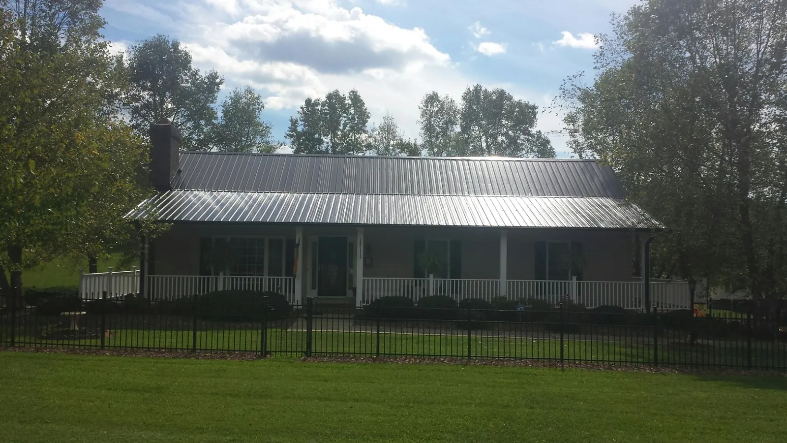 Gray metal roof on a brick ranch with a full width front porch — Gutter Guard Installation work by our crew in Lima