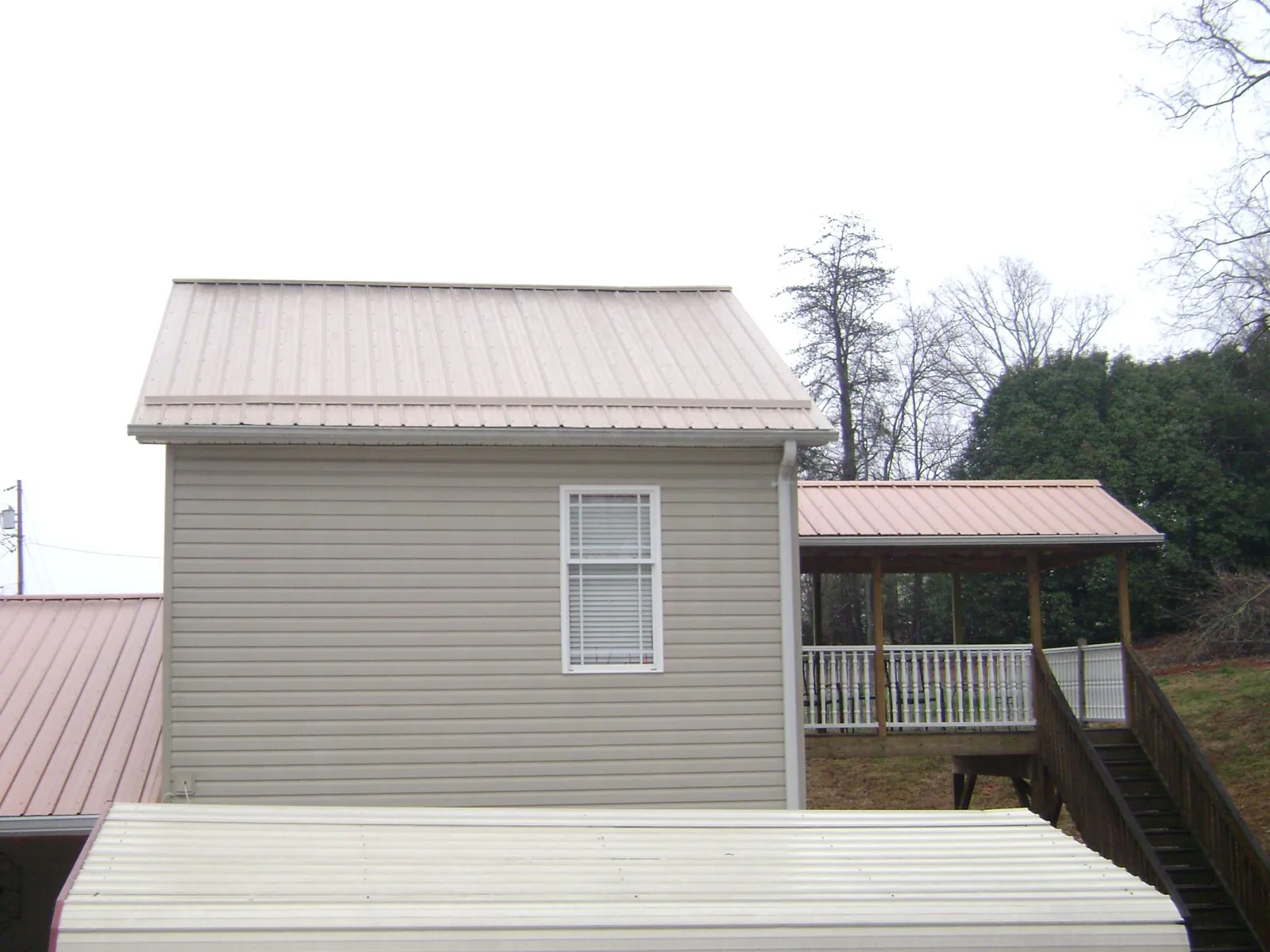 Tan metal roofs on a two story addition and attached porch, from a Roof Replacement job in Lima